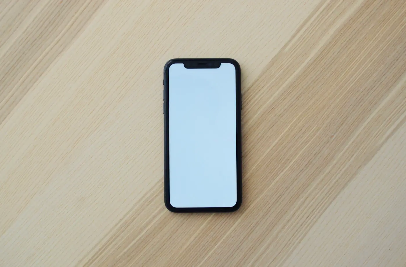 A phone with a blank screen resting on a wooden desk