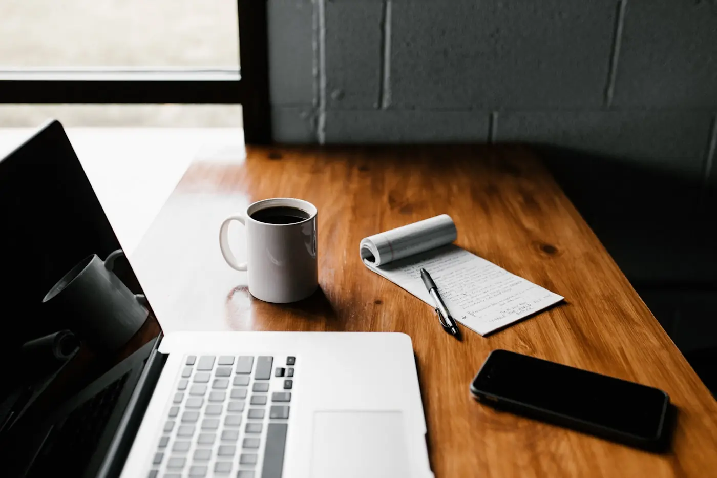 A laptop, notepad and phone on a wooden desk